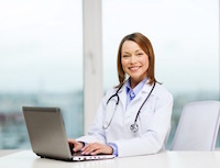 Picture of a female Physicians sitting at a desk wth a laptop open. She is smiling.
