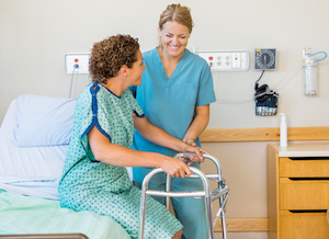 Picture a female Nurse helping a female patient get up of a swing bed using a walker.