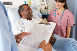 Picture of male patient sitting up in a swing bed smiling at a female nurse that is standing next to his bedside. She is smiling as well.