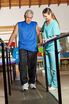 Picture of a female Physical Therapist helping a man walk that is holding on to railing in a Physical Therapy gym.