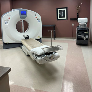Picture of an MRI machine. There is a patient lying down in the MRI scanner with their hands up above their head. There is a female Nurse standing next to the patient on the side of the MRI scanner.